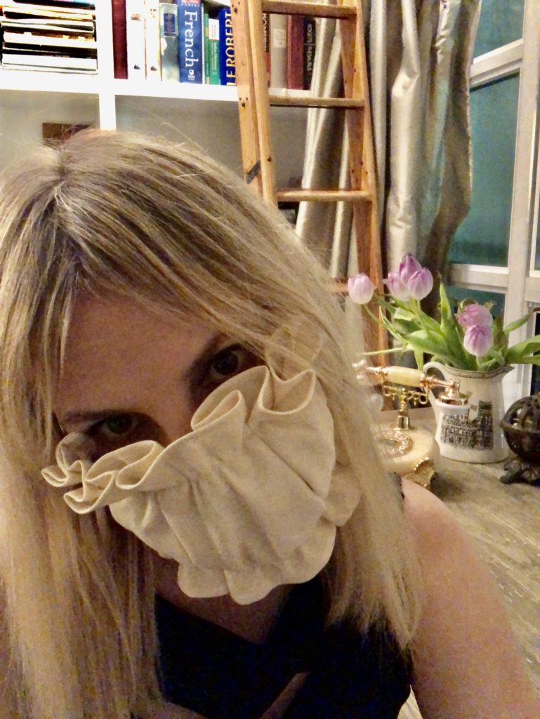 A selfie of Ardra wearing a ruffled Covid mask. She is in her library.