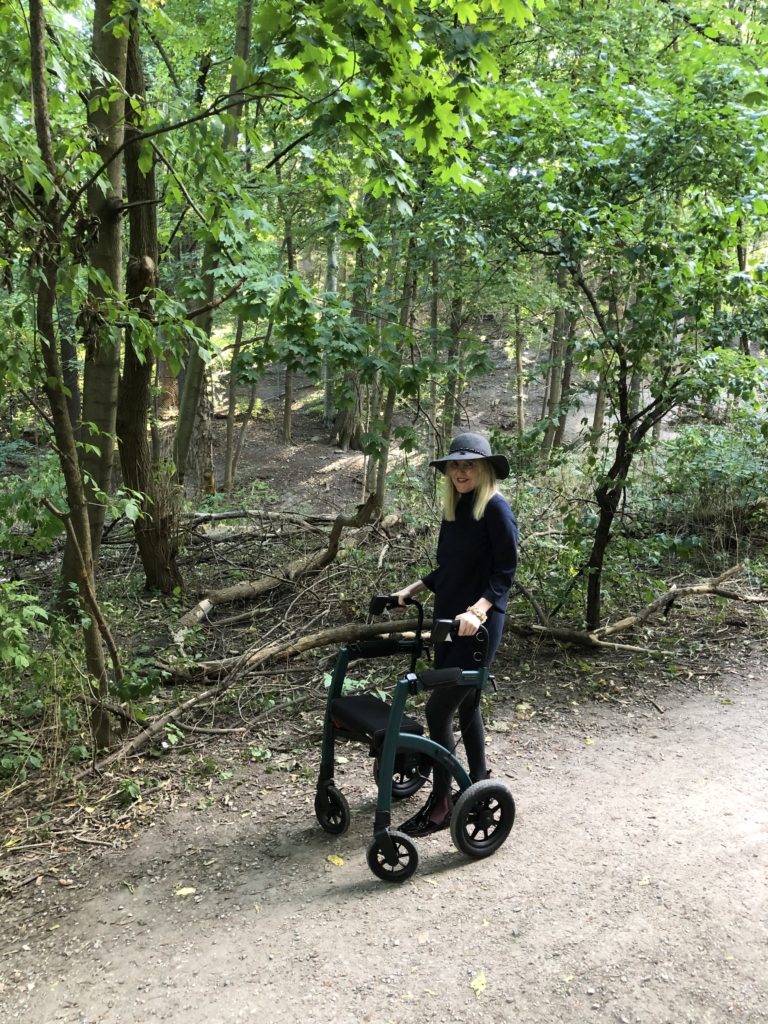 Ardra stands with her Rollz Performance in rollator mode. She is enjoying being able to be comfortably off-road on difficult terrain.