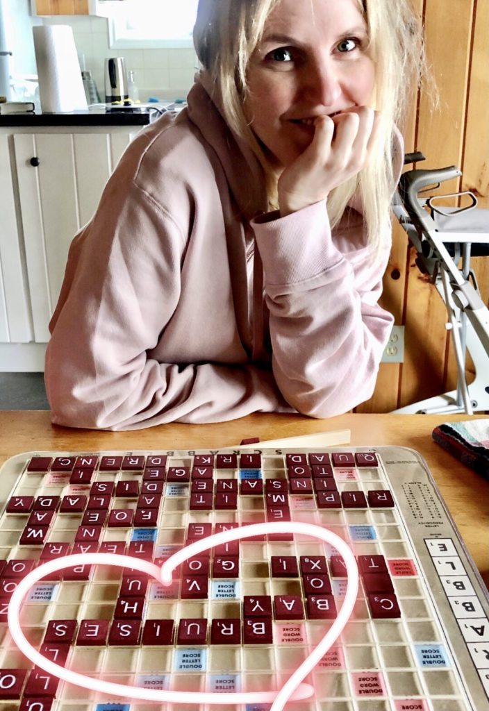 A woman smiles over a Scrabble board. The word "bruises" is circled as a nod to how MS can lead to bruises. 