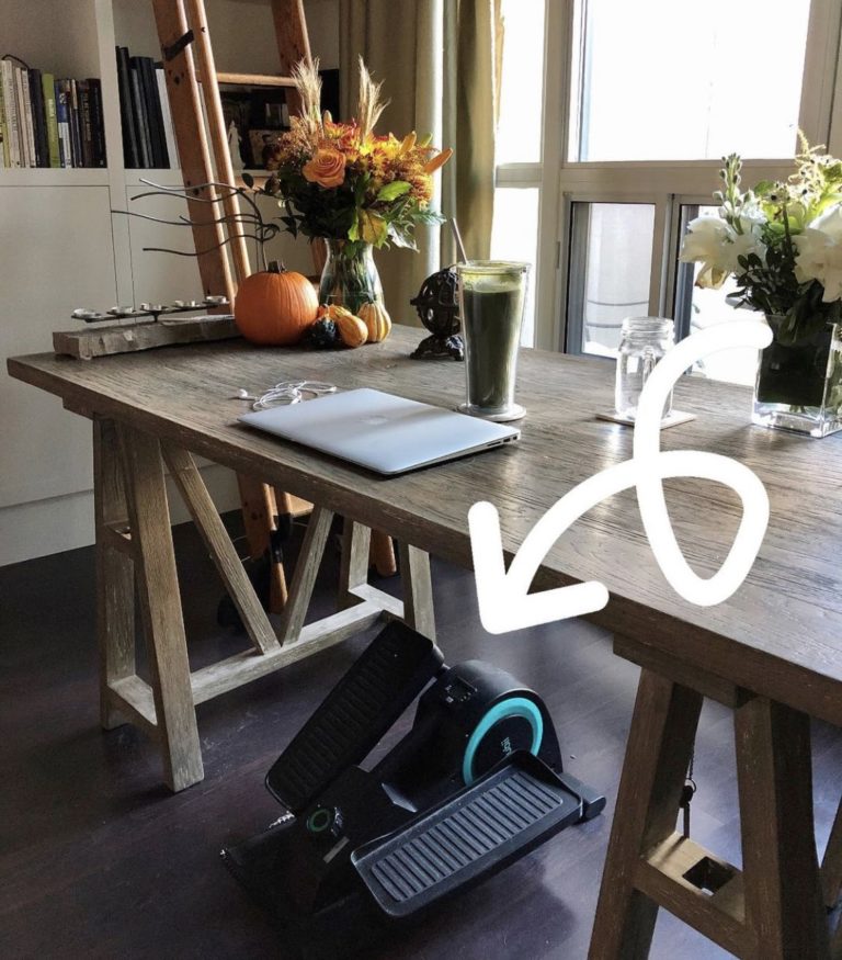 Underneath a wooden table is a small elliptical machine. It's a great gift for someone with MS who has expressed an interest in getting more cardio exercise.
