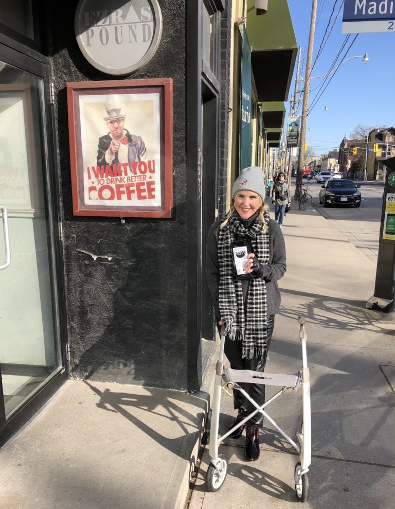 Ardra stands in front of Ezra's pound, her neighbourhood coffee shop. She is standing with her sleek and stylish byAcre rollator, looking like a total babe with a mobility aid. 
