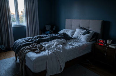 Bed with rumpled white and dark gray linens, bedside table with red digital clock reading 5:30 and a white mug